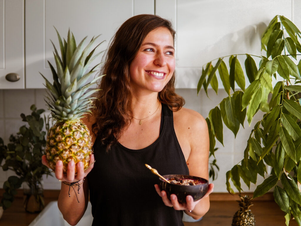 Frau hält Ananas in der rechten und Smoothie Bowl in der linken Hand