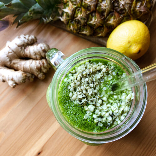 Green Smoothie im Glas daneben eine Ananas, Zitrone und Ingwer