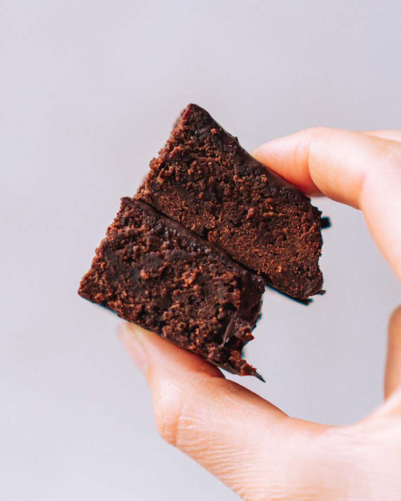 2 Schokoladenbrownies zwischen Daumen und Zeigefinger gehalten