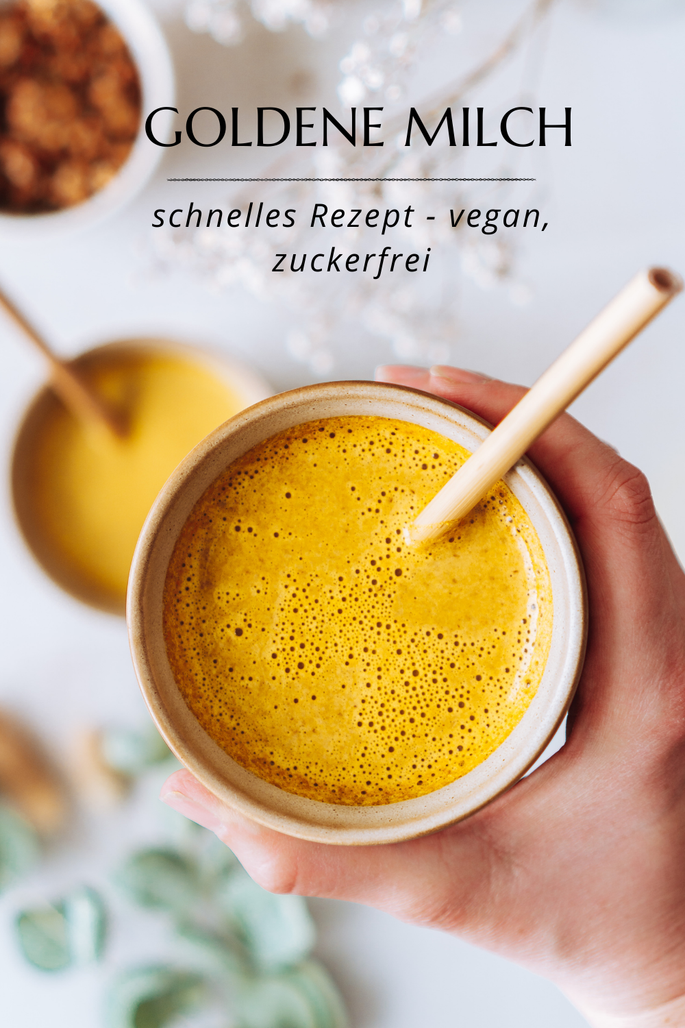 2 Tassen mit Goldener Milch, eine davon in einer Hand hoch gehalten von oben Fotografiert